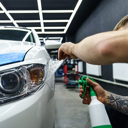 Técnico aplicando película de proteção de pintura PPF em um veículo premium